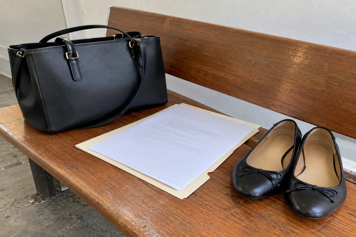 An interview bag, a printed résumé in a plain folder and a pair of flat leather shoes on a bench