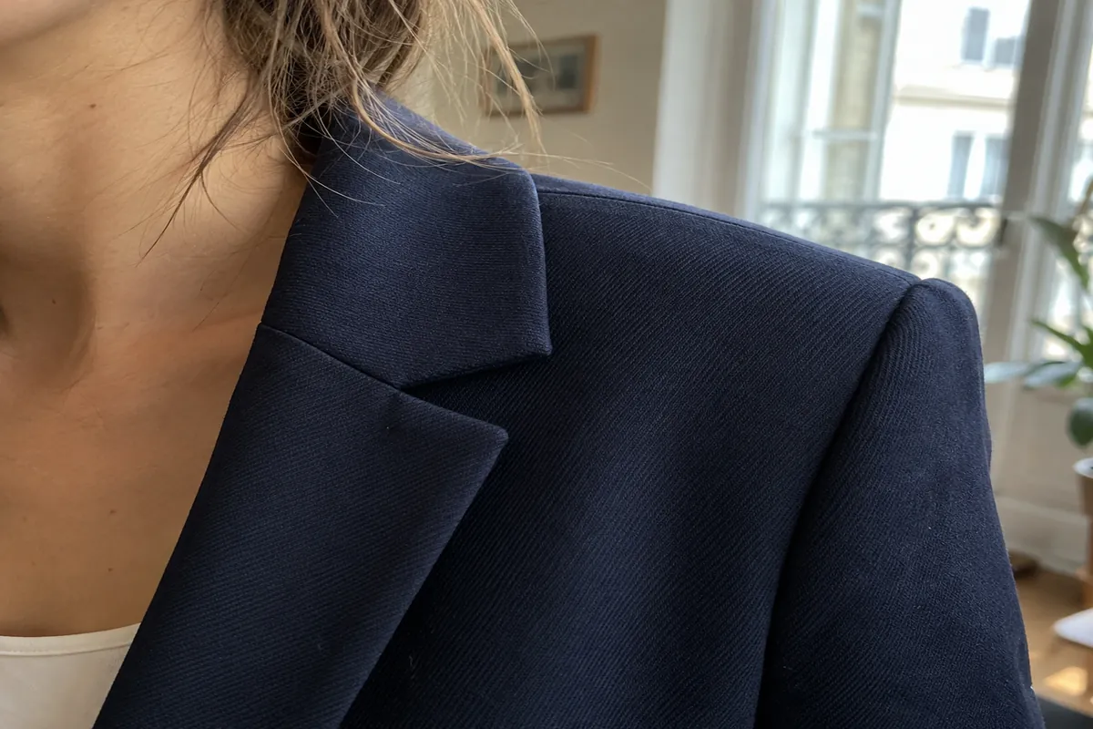 A close view of a jacket collar and shoulder seam on a woman in a navy suit, in soft window light